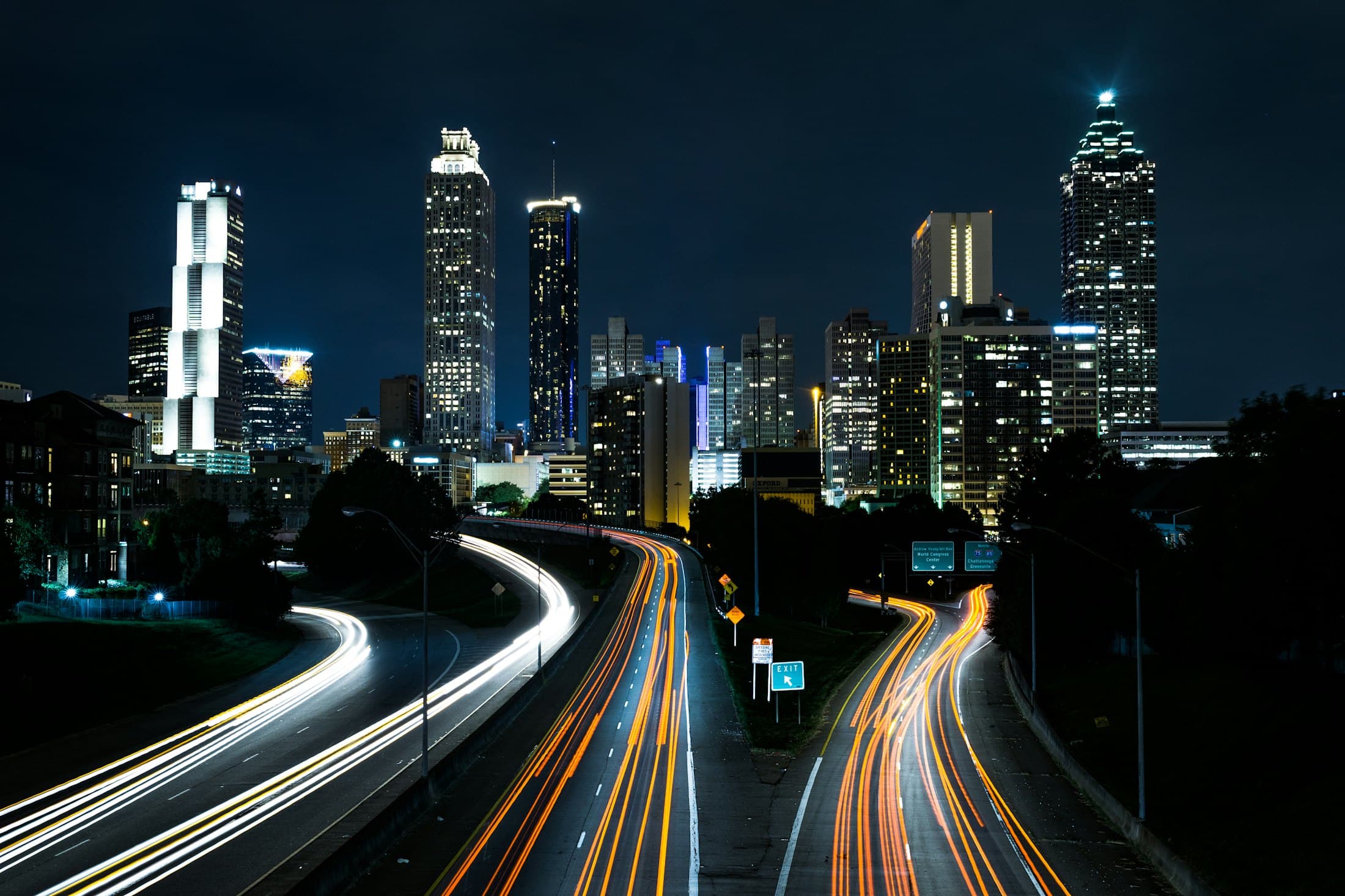 City skyline at night, light trails tracing movement between illuminated towers